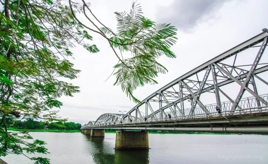 The steel arches of Trường Tiền Bridge over the Hương River, framed by green leaves
