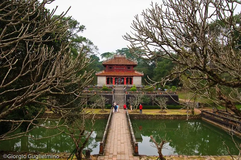 A stone causeway crossing a lotus pond towards a pavilion at Minh Mạng’s tomb